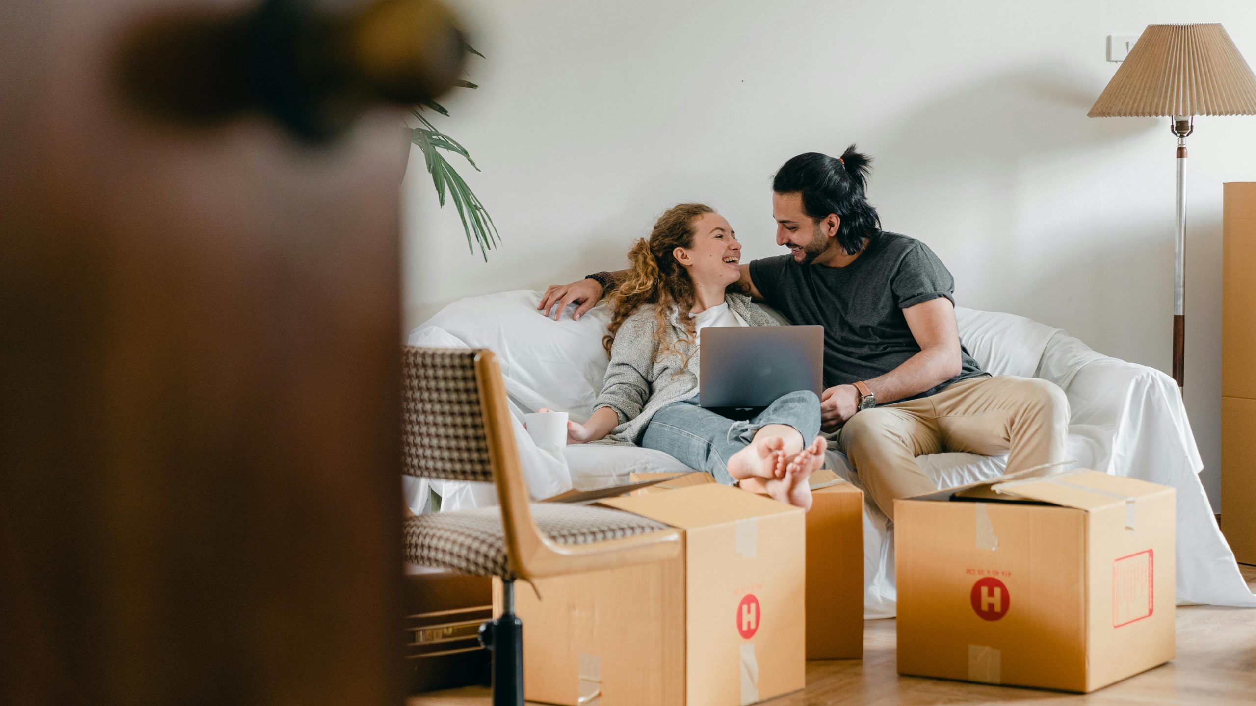 Couple sat on a sofa on laptop surrounded by moving boxes